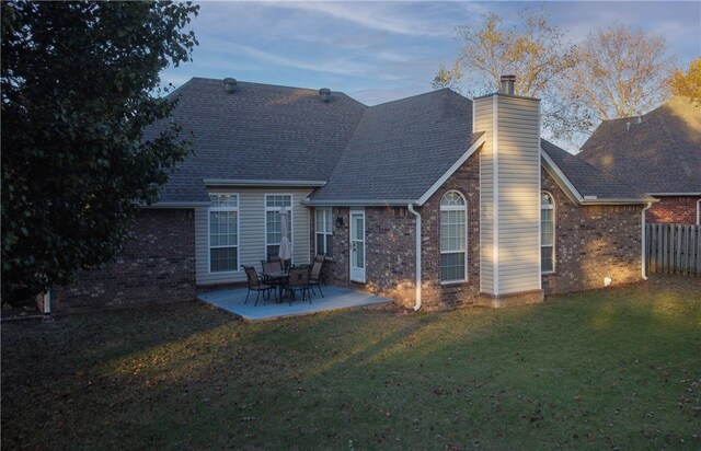 back house at dusk featuring a lawn and a patio area