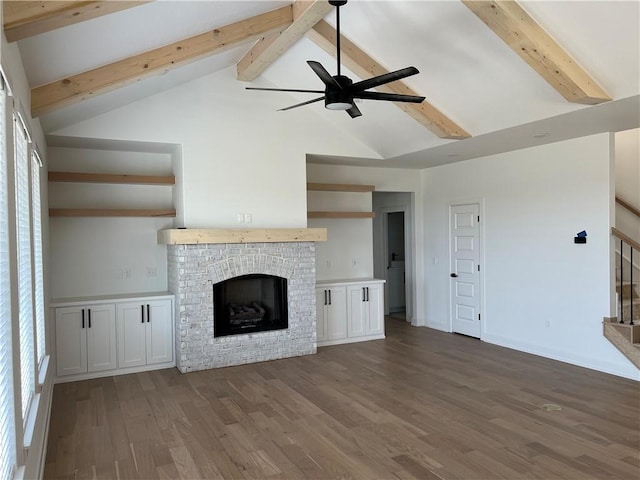 unfurnished living room featuring beam ceiling, dark hardwood / wood-style floors, a brick fireplace, and ceiling fan