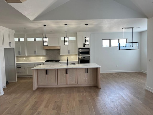 kitchen featuring white cabinets, light stone counters, an island with sink, and lofted ceiling