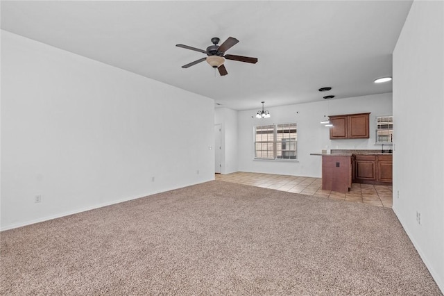 unfurnished living room featuring ceiling fan with notable chandelier and light colored carpet