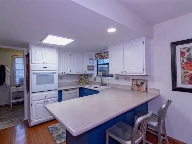 kitchen featuring kitchen peninsula, white cabinetry, white appliances, and sink