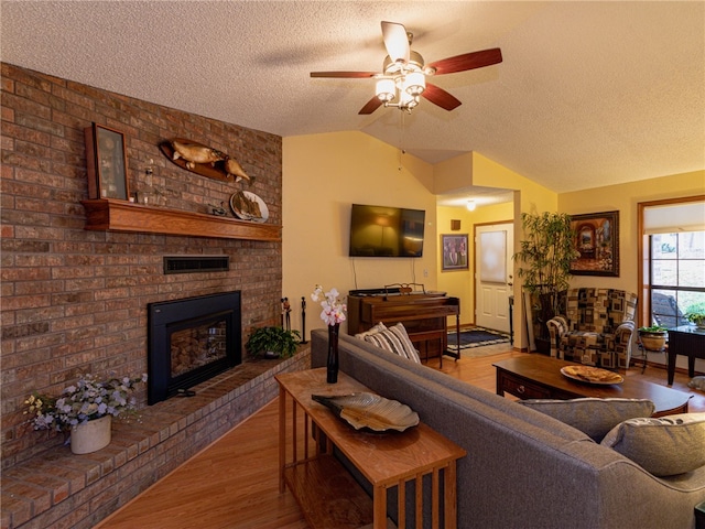 living room with ceiling fan, hardwood / wood-style floors, a textured ceiling, lofted ceiling, and a fireplace