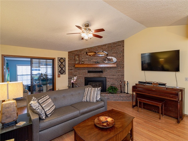 living room featuring a brick fireplace, a textured ceiling, ceiling fan, light hardwood / wood-style floors, and lofted ceiling