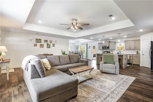 living room with ceiling fan with notable chandelier, dark hardwood / wood-style floors, and a raised ceiling