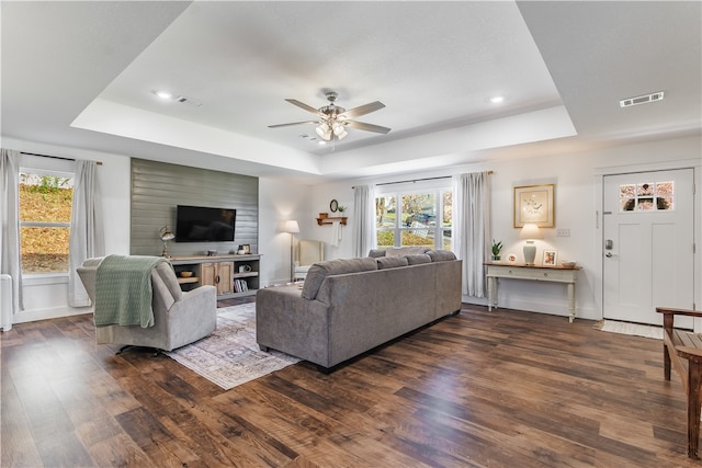 living room featuring a tray ceiling, ceiling fan, and dark wood-type flooring