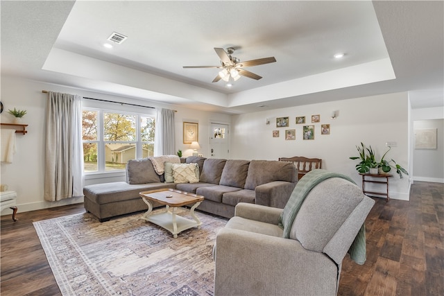 living room with a raised ceiling, ceiling fan, and dark wood-type flooring