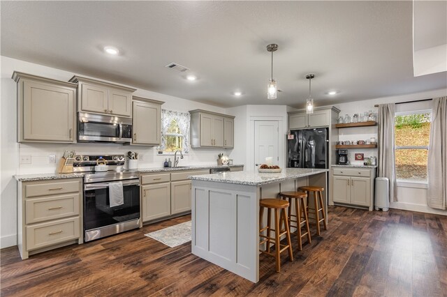 kitchen with sink, appliances with stainless steel finishes, a kitchen island, dark hardwood / wood-style flooring, and a breakfast bar area