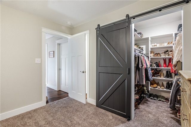 walk in closet with a barn door and dark carpet