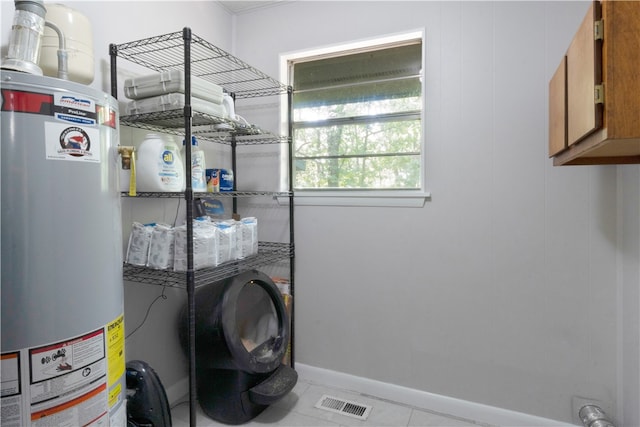 laundry room featuring cabinets, light tile patterned floors, and gas water heater