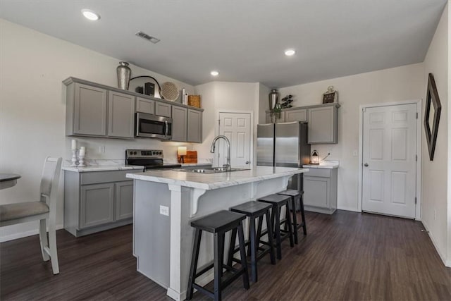 kitchen with gray cabinetry, stainless steel appliances, dark hardwood / wood-style floors, a breakfast bar area, and a center island with sink