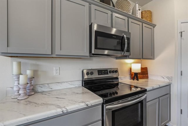 kitchen featuring stainless steel appliances, light stone counters, and gray cabinetry