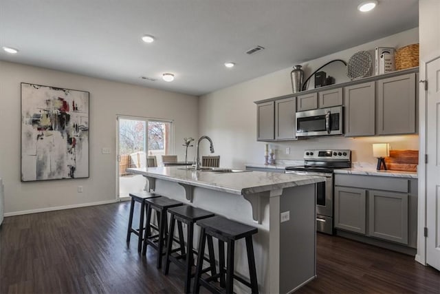 kitchen with appliances with stainless steel finishes, dark hardwood / wood-style floors, gray cabinetry, and an island with sink