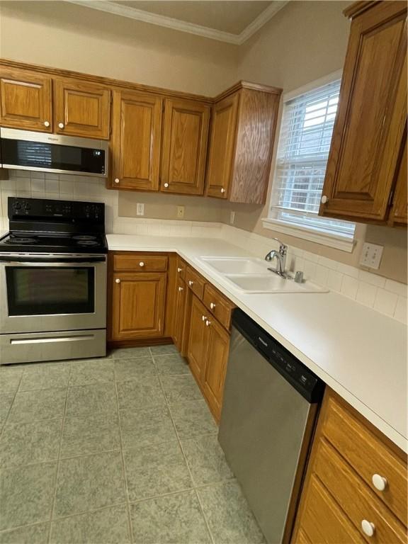 kitchen with decorative backsplash, appliances with stainless steel finishes, crown molding, sink, and light tile patterned floors