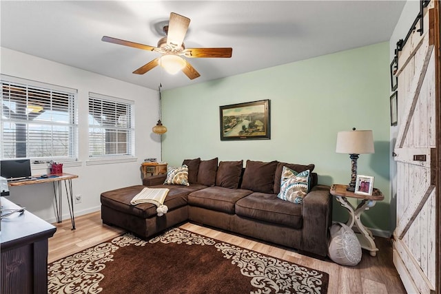 living room featuring a barn door, light wood-type flooring, and ceiling fan