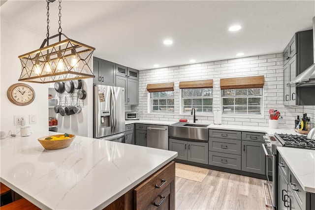 kitchen with sink, decorative backsplash, hanging light fixtures, stainless steel appliances, and light stone countertops