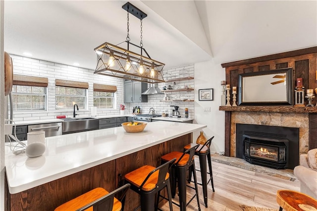 kitchen with a kitchen bar, sink, stainless steel dishwasher, pendant lighting, and wall chimney range hood