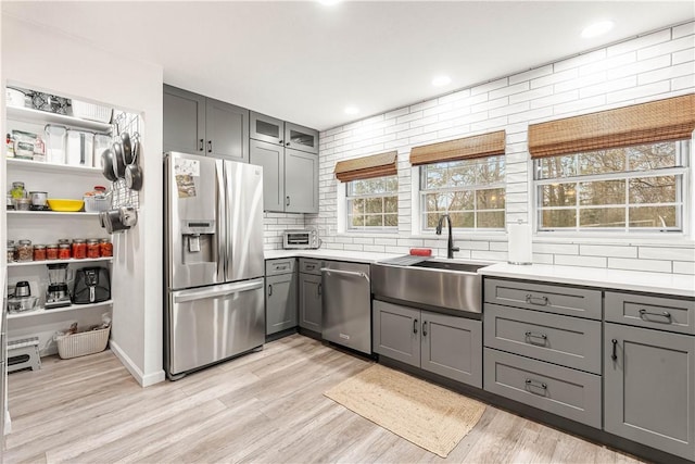 kitchen featuring sink, gray cabinetry, backsplash, stainless steel appliances, and light hardwood / wood-style floors