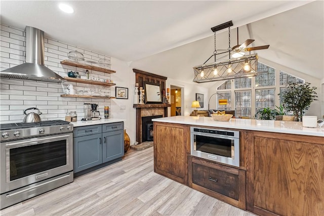 kitchen featuring appliances with stainless steel finishes, decorative light fixtures, lofted ceiling with beams, tasteful backsplash, and wall chimney exhaust hood