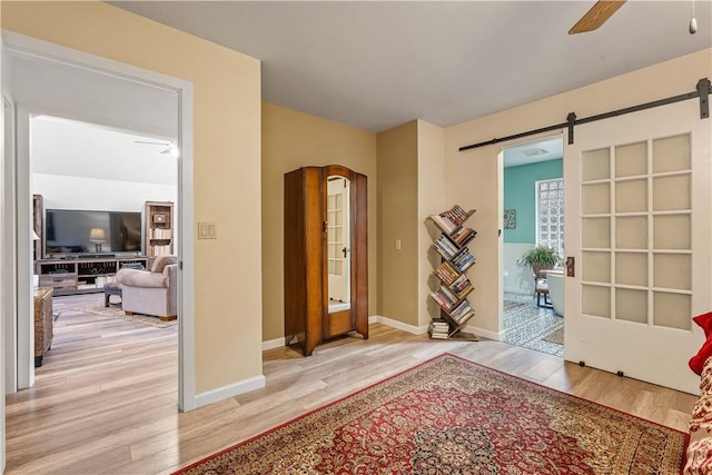 foyer entrance featuring ceiling fan, a barn door, and light hardwood / wood-style flooring