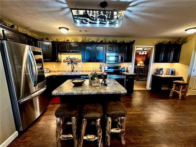 kitchen featuring a center island, sink, a textured ceiling, light stone counters, and stainless steel appliances