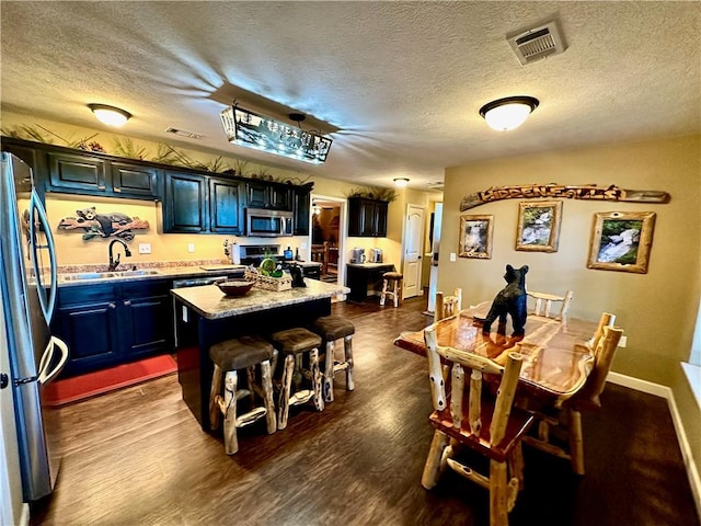 kitchen featuring a center island, sink, dark wood-type flooring, stainless steel appliances, and a textured ceiling