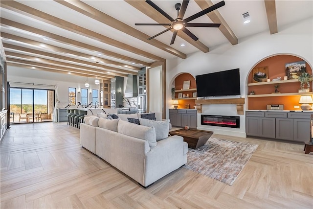 living area featuring visible vents, ceiling fan, built in features, beam ceiling, and a glass covered fireplace