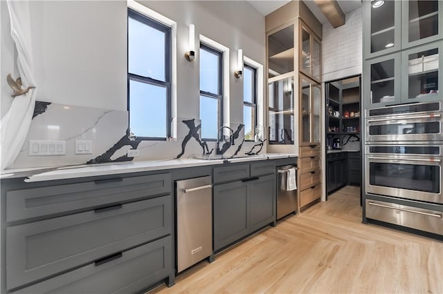 kitchen featuring a warming drawer, gray cabinetry, tasteful backsplash, appliances with stainless steel finishes, and glass insert cabinets