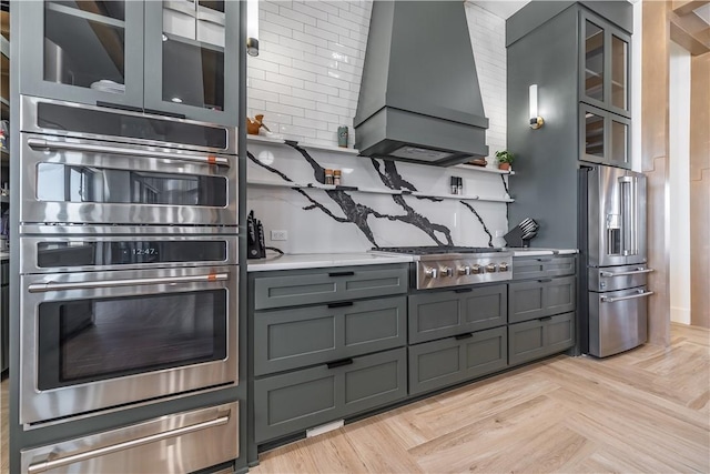 kitchen with a warming drawer, gray cabinetry, light countertops, appliances with stainless steel finishes, and wall chimney range hood