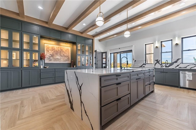 kitchen with beam ceiling, a kitchen island with sink, a sink, light stone countertops, and dishwasher