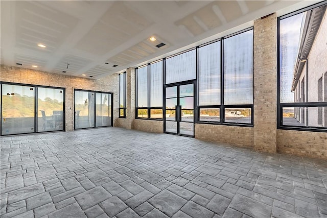 empty room featuring visible vents, stone finish floor, and brick wall