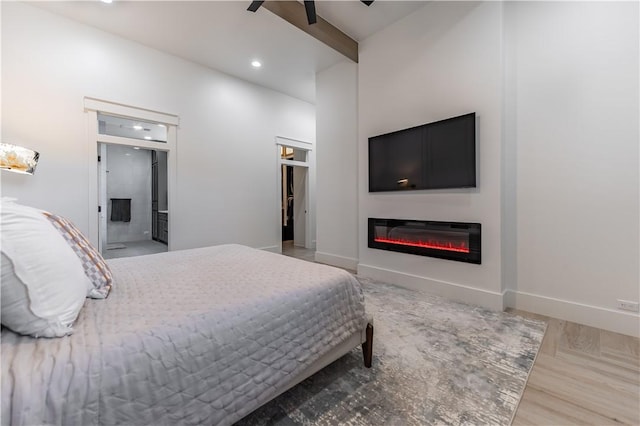 bedroom featuring beam ceiling, wood finished floors, a glass covered fireplace, recessed lighting, and baseboards