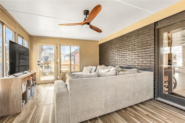 living room featuring ceiling fan, light hardwood / wood-style flooring, and brick wall