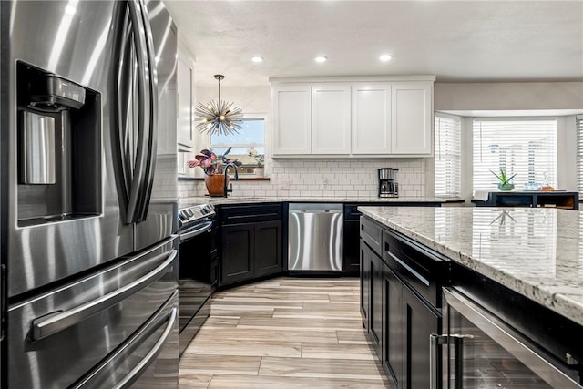 kitchen with hanging light fixtures, light hardwood / wood-style flooring, light stone countertops, white cabinetry, and stainless steel appliances