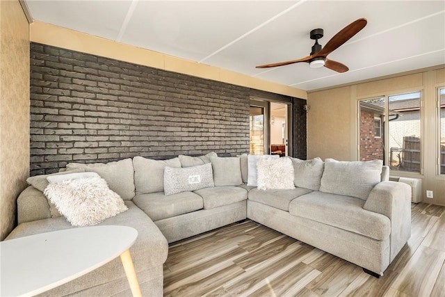 living room featuring ceiling fan, hardwood / wood-style floors, and brick wall