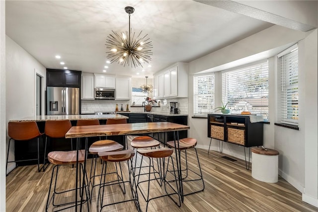 kitchen featuring light hardwood / wood-style flooring, backsplash, a chandelier, white cabinets, and appliances with stainless steel finishes