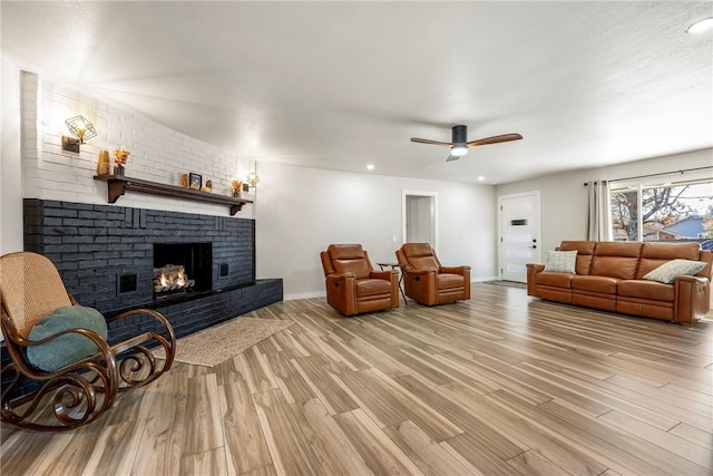 living room with a fireplace, light wood-type flooring, and ceiling fan