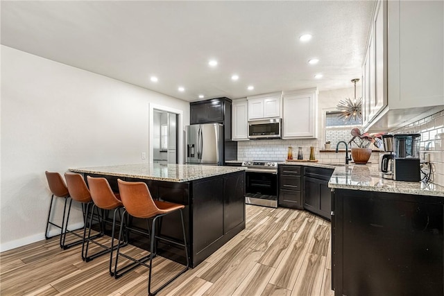 kitchen featuring white cabinets, sink, appliances with stainless steel finishes, decorative light fixtures, and light hardwood / wood-style floors