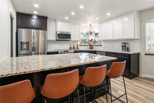 kitchen with backsplash, stainless steel appliances, white cabinetry, and light hardwood / wood-style floors