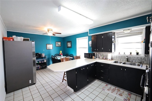 kitchen featuring stainless steel refrigerator, ceiling fan, sink, kitchen peninsula, and a breakfast bar