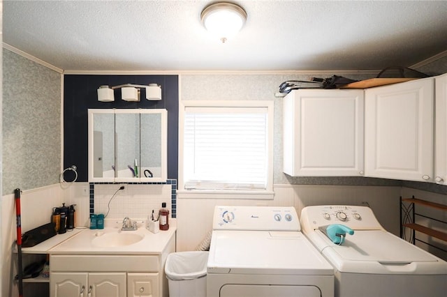 laundry room featuring cabinets, sink, ornamental molding, a textured ceiling, and washing machine and clothes dryer