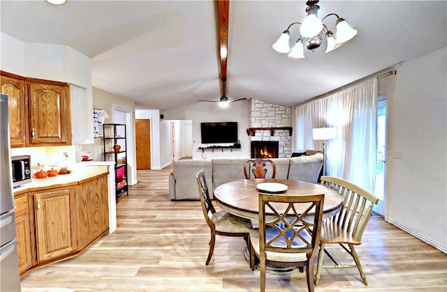 dining space with ceiling fan with notable chandelier, lofted ceiling with beams, a fireplace, and light wood-type flooring