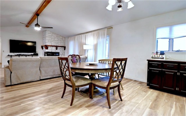 dining space featuring vaulted ceiling with beams, ceiling fan, a stone fireplace, and light hardwood / wood-style flooring