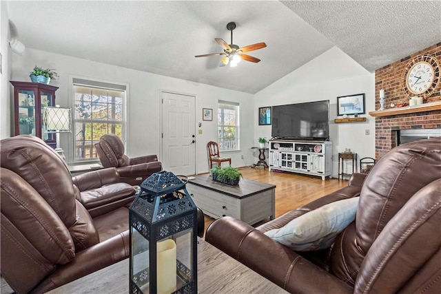living room featuring vaulted ceiling, a ceiling fan, wood finished floors, a wealth of natural light, and a brick fireplace
