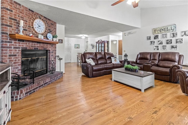 living room with light wood-type flooring, a brick fireplace, a textured ceiling, ceiling fan, and lofted ceiling