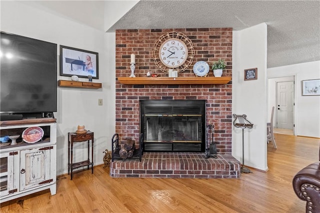 living area featuring a textured ceiling, wood finished floors, a brick fireplace, and baseboards