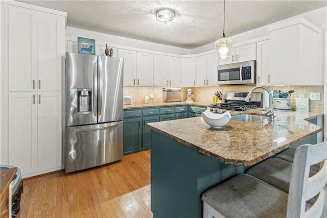 kitchen featuring a kitchen breakfast bar, stainless steel appliances, a sink, a peninsula, and light wood-style flooring
