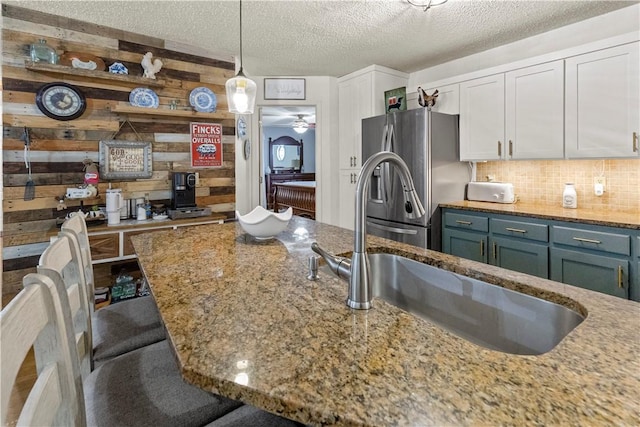 kitchen with a sink, a textured ceiling, wooden walls, and stainless steel fridge