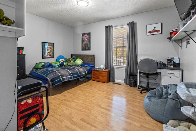 bedroom with wood finished floors, a textured ceiling, and visible vents