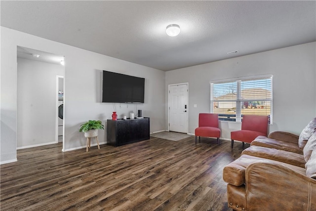 living room with dark wood-type flooring, a textured ceiling, and washer / dryer