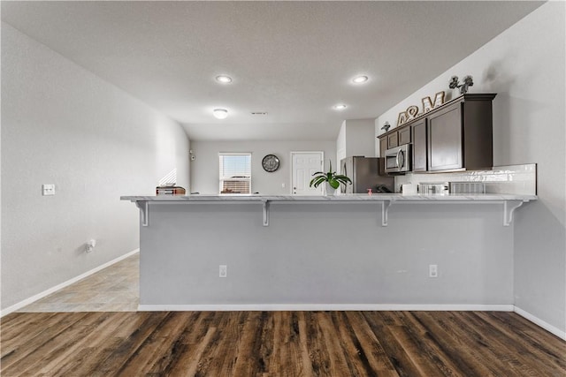 kitchen with a kitchen bar, kitchen peninsula, dark hardwood / wood-style flooring, and appliances with stainless steel finishes